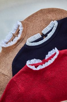 three sweaters with lace on them are sitting next to each other in different colors