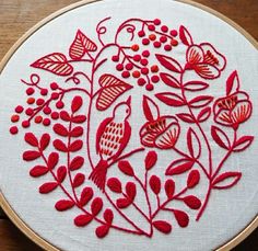 a close up of a embroidery on a wooden hoop with red flowers and leaves in it