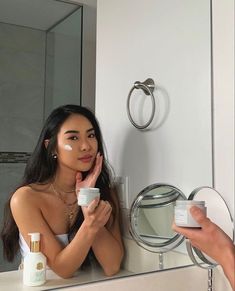 a woman is looking at her reflection in the mirror while she brushes her teeth and holds a cup