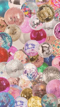 many shiny disco balls hanging from the ceiling in different colors and sizes, all grouped together