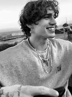 a young man with curly hair and tattoos on his arm smiles at the camera while sitting in a chair