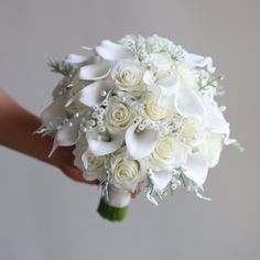 a bridal bouquet with white roses and baby's breath is being held by someone