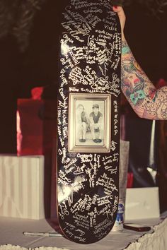 a man holding up a skateboard with autographs on the board and writing all over it