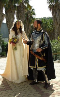 a man and woman dressed up in medieval clothing standing next to each other with palm trees behind them