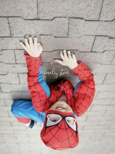 a young boy wearing a spider - man costume and holding his hands up in the air