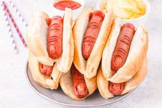 three hotdogs on buns with ketchup and mustard in small bowls