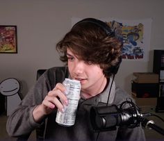 a young man drinking from a can while sitting in front of a camera with headphones on