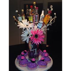 a vase filled with cupcakes and flowers on top of a table next to bottles