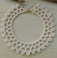 a white necklace with pearls and gold chains on a wooden table next to a leaf