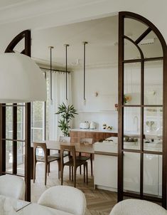 an open kitchen and dining room area with white walls, wood flooring and large arched windows