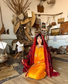 a woman sitting on the floor in an orange dress and red shawl over her head