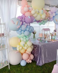 a bunch of balloons are hanging from the ceiling in front of a table with a purple cloth on it