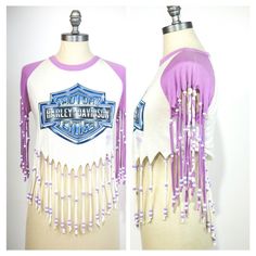 Vintage 1980s womens beaded fringe Harley Davidson t-shirt. Features Blue and purple faux chrome Harley Davidson logo on a white background with purple and white beaded fringe at sleeves and bottom edge. With crew neckline, purple raglan sleeves, and super soft feel.   Polyester/cotton blend stretch fabric Excellent vintage condition Tag says: original brand tag missing, no size listed Bust: 34 inches Waist: 31 inches Bottom edge: free Length: 23.5 inches (including fringe) Sleeve: 18 inches (including fringe) Beaded Fringe Tshirt, White Cotton Fringe Tops, Fitted White Tops With Fringe, White Fitted Fringe Tops, Logo Harley Davidson, Cut Shirt Designs, Diy Cut Shirts, Fringe Tshirt, Harley Davidson Vintage