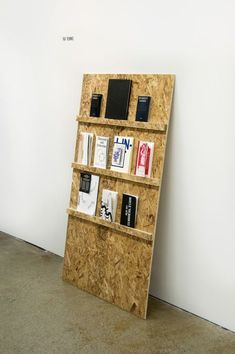 a wooden shelf with books and other items on it next to a white wall in an empty room