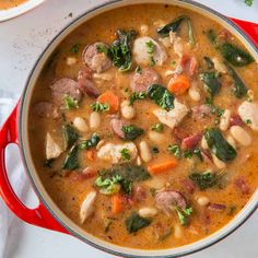 a red pot filled with soup and vegetables on top of a white countertop next to a plate of food