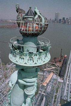 the top of a tall building with a statue on it's side and a city in the background