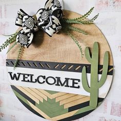 a welcome sign hanging on the side of a brick wall next to a green cactus