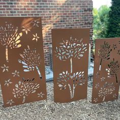 three metal panels with trees on them in front of a brick wall and some grass