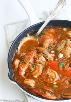 a skillet filled with shrimp and tomato soup on top of a white table cloth