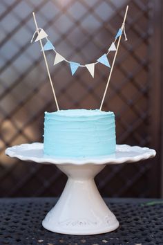 a blue cake sitting on top of a white cake plate with bunting and flags