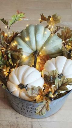 a bucket filled with white pumpkins and greenery on top of a wooden floor