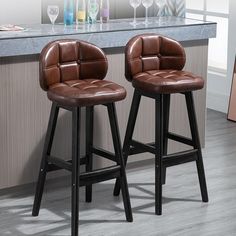 two brown leather bar stools sitting in front of a counter with wine glasses on it