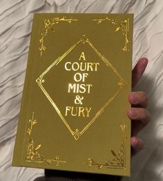 a court of mist and fury book being held up by someone's hand on a bed