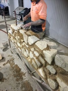 a man in an orange shirt is working on a stone wall made out of rocks