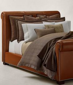 a bed with brown and white sheets, pillows and blankets on top of it's headboard