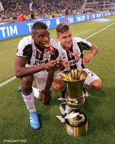 two soccer players kneeling next to a trophy