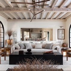 a living room filled with lots of furniture next to tall black framed windows and wooden beams