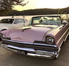 two old cars parked next to each other in a parking lot near water and trees