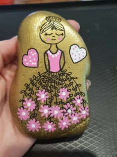 a hand holding a painted rock with a girl in a dress and flowers on it