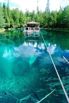 a boat floating on top of a lake surrounded by trees and blue water with clouds in the sky