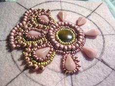 a pink and green beaded brooch sitting on top of a piece of cloth