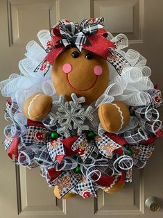 a christmas wreath with a teddy bear on it hanging from the front door, decorated with ribbon and bows