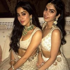 two beautiful young women sitting next to each other on a white couch with gold jewelry