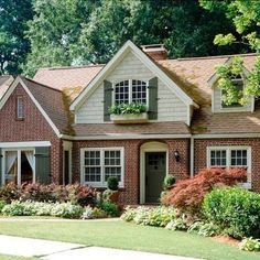 a brick house with green shutters and white trim on the front door is surrounded by lush greenery