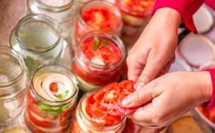 two hands picking tomatoes from jars filled with water and other food in the back ground