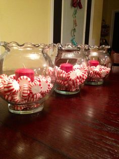 three glass vases filled with candy canes on top of a wooden table