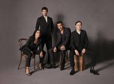 three men and one woman are posing for a photo in front of a gray background