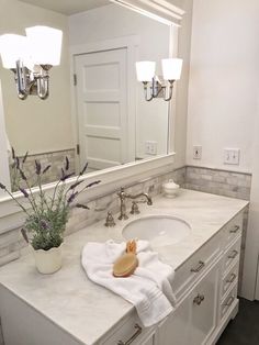 a white bathroom with two sinks and a large mirror above the sink is decorated with purple flowers