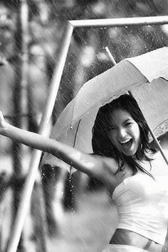 a woman holding an umbrella in the rain with her arms out and smiling at the camera