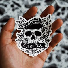 a hand holding a sticker with a skull wearing a hat and the words not everyone's cup of tea on it