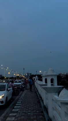 cars parked on the side of a road next to a white fence and light poles