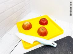 an apple tray with three apples on it and a knife sitting next to the tray