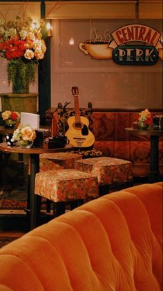 an orange couch and table in a room with flowers on the wall behind it, and a guitar hanging from the ceiling