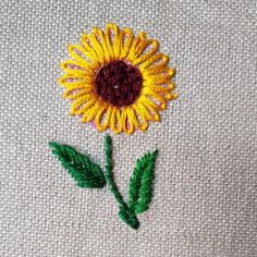 a yellow flower with green leaves is embroidered onto a white piece of cloth that has been stitched together