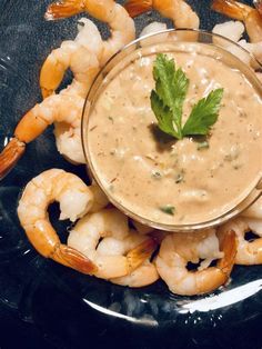 a black plate topped with shrimp and dip surrounded by garnish on top of it