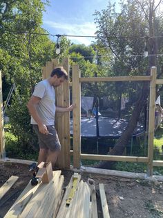 a man standing on top of a wooden platform in the middle of a yard next to a fence